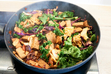 Colorful vegan stir fry with tofu, kale, cabbage, and carrots in a hot pan. A healthy and nutritious dish, full of vibrant vegetables and plant-based protein.