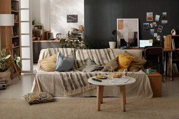 Small round table with french fries and hamburgers on plates, drinks, magazine and remote control standing in front of couch
