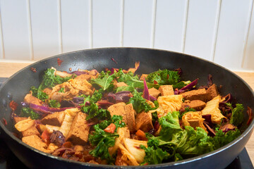Colorful vegan stir fry with tofu, kale, cabbage, and carrots in a hot pan. A healthy and nutritious dish, full of vibrant vegetables and plant-based protein.