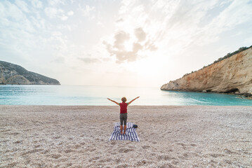 Woman performing yoga exercises on a beautiful empty beach in Greece. Dramatic coastline scenic bay rocky cliffs in the Ionian islands.