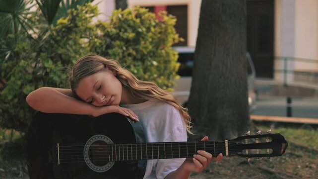 Young Musician Play Acoustic Guitar While Sitt on Bench in Park, Enjoy Summer Day Surrounded by Nature. Street Musician