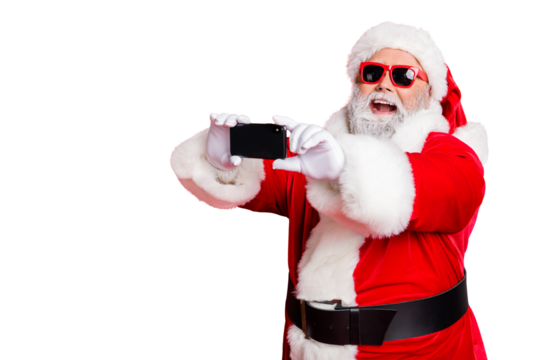 Portrait of excited santa claus in eyewear making selfie with cell phone device on christmas vacation smiling wearing belt isolated over red background - Powered by Adobe
