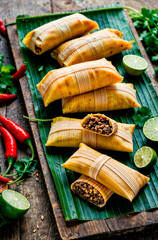 Traditional tamales wrapped in banana palm leaves, arranged on a rustic wooden board