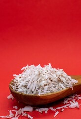 Grated Coconut White Flesh in a Wooden Spoon Isolated on Red Background with Copy Space for Texts Writing
