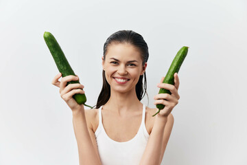 Young woman holding cucumbers with a cheerful smile, showcasing healthy eating and natural beauty...