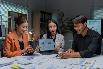 Team of young asian professionals are discussing a project, collaborating on a laptop and reviewing paperwork with financial charts and graphs