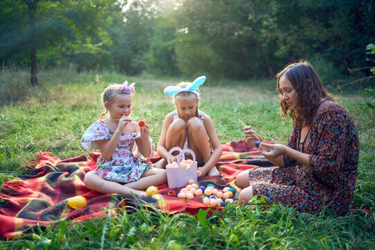 two little girls and mom paint eggs at easter picnic
