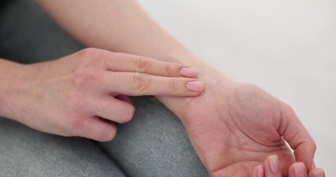 Woman puts fingers onto wrist checking pulse sitting on sofa. Attentive female monitors health condition feeling overall fatigue in morning