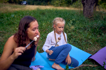 mother and her daughters  roasting and eating marshmallows on the campfire, camping vacation with children, mosquito bites on children's faces