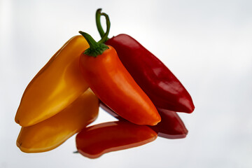 An assortment of red, orange and yellow sweet peppers on a mirror with a white background.