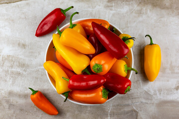 An assortment of red, orange and yellow sweet peppers in a white bowl with a neutral tile background.  Top down view.