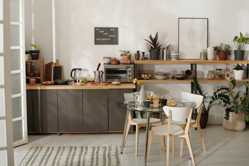 Part of spacious cozy kitchen with counter and shelves by wall with posters and round table with several chairs standing around