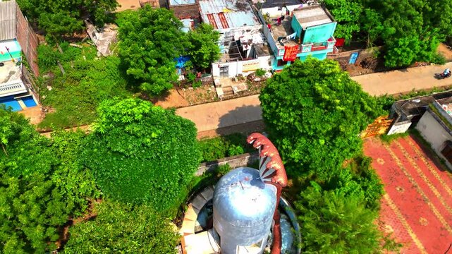 A big Shivling figurine stands in the Hindu temple, surrounded by trees and nearby village houses