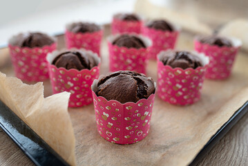 Brown chocolate muffins wrapped in white paper baked in the oven, lying on baking paper.
