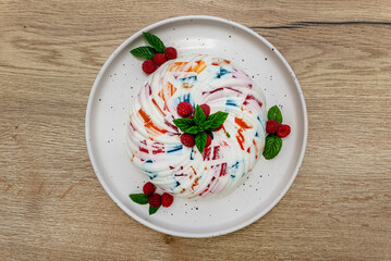 Dessert made of white and colored jelly, decorated with mint leaves and raspberries.