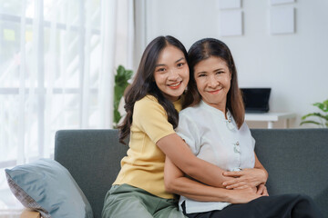 Young woman is hugging her mother from behind, both are smiling and looking happy