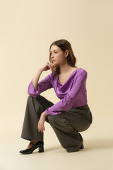 Female model wearing purple silk blouse and tailored grey trousers. Classic and timeless simple fashion. Studio shot.