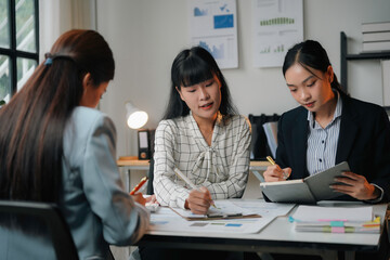Three asian businesswomen are having a meeting in the office and analyzing financial documents using a calculator