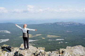 A person stands triumphantly on a mountain peak, arms spread wide in joy, reveling in the...