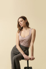 Female model wearing cream sleeveless blouse and tailored grey trousers. Classic and timeless simple fashion. Studio shot.