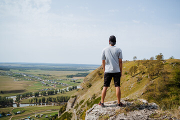 A man is confidently standing on top of a majestic mountain while gazing out over a beautiful...