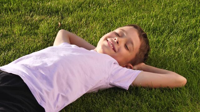 happy child lie on the grass in park. happy face child in sun. child relaxing on the grass enjoying nature. moments of life