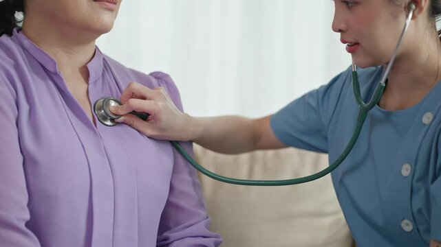 Asian senior elder female patient sitting on sofa in living room using dumbbells exercise,check up with caregiver at home nursing care.Asian older woman doing physiotherapist with support from nurse.