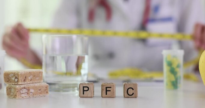 Abbreviation PFC on wooden cubes and female doctor with tape measure in hospital. Woman nutritionist chooses diet for patient weight loss