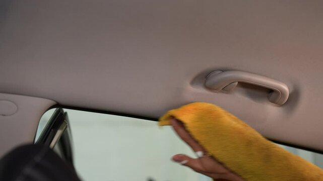 Car detailer using yellow cloth to meticulously clean car ceiling, achieving flawless result. Process of enhances appearance and maintenance of vehicle during professional detailing, slow motion