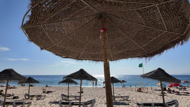 A beach scene in Comporta, Portugal, with a straw umbrella casting shadow on the sand.
