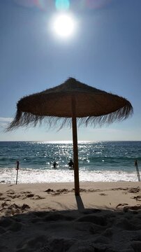 A beach scene in Comporta, Portugal, with a straw umbrella casting shadow on the sand.
