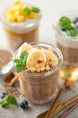 Chocolate chia pudding from coconut milk with mango,  blueberries and banana in a glasses.
