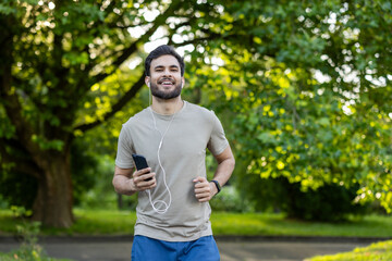 Smiling Indian man in headphones and phone running in the park and doing sports