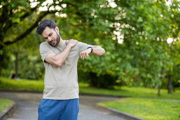 Indian young man exercising in the park, doing a morning run, holding his hand on his shoulder and...