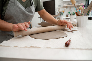 Preparing clay for cutting and assembling it. Slab building method in ceramics crafting. Using a wooden stick to roll out a flat sheet of clay.