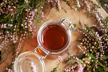 Herbal syrup in a glass jar with fresh wild heather flowers harvested in the forest
