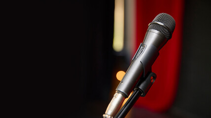 A microphone is positioned on a stand in front of a striking red curtain. A banner for the text.