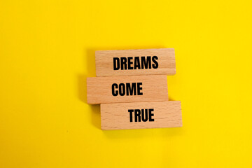 Dreams come true message written on wooden blocks with yellow background. Conceptual dreams come...