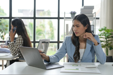 Young businesswoman feeling stressed and having neck pain while working on a laptop in the office