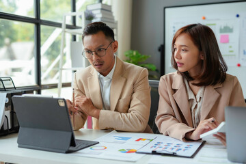 Business partners reviewing financial data on a tablet, engaged in a focused discussion about market trends and company performance