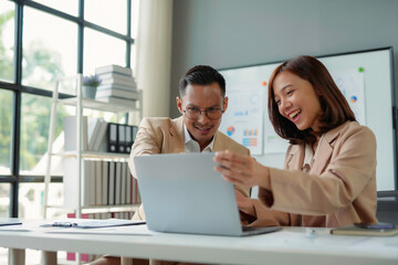Two business partners are smiling and discussing a project, looking at laptop screen in modern...