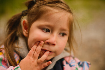 Portrait of a small girl with ponytails in a jacket. Grimaces. Emotions. Autumn