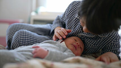 Older brother interacting gently with newborn sibling, both lying on a bed with floral blankets, illustrating a tender moment of bonding and early connection between siblings