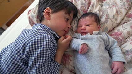 Obraz premium Older brother lying side by side with newborn sibling on a bed, sharing a close and heartwarming moment of bonding that emphasizes the love and affection between the two siblings