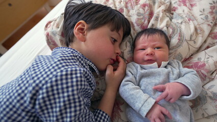 Obraz premium Older brother lying side by side with newborn sibling on a bed, sharing a close and heartwarming moment of bonding that emphasizes the love and affection between the two siblings
