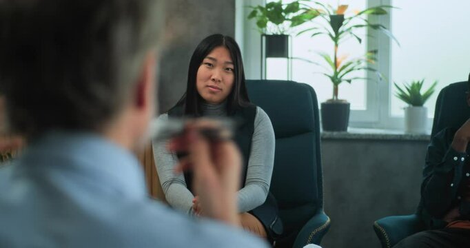 Asian young woman discusses relationship problems. Multiethnic couple on counseling session with psychologist. In the foreground, unfocused psychotherapist talks to young family during couples therapy