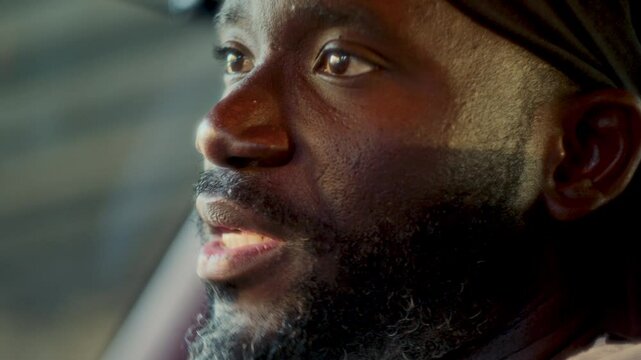 Close-up view of bearded African American man wearing durag sitting in car and talking to friends