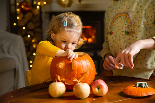 Father his toddler and daughter carving pumpkin jack o lantern, Halloween celebration at home. Fun craft and decoration at home. Happy children and their dad preparing for the holiday, decorating the
