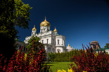 A large white building with gold domes is amid trees and bushes