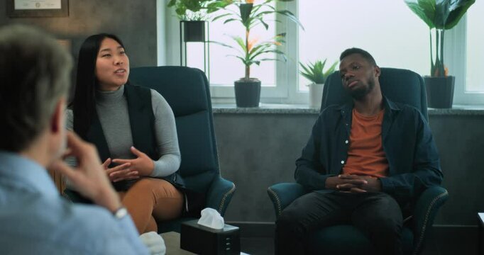 Multiethnic couple sit on chairs, discuss relationship problems with psychologist on counseling session. Back view of therapist providing couples therapy to young family. Psychology and sexology.